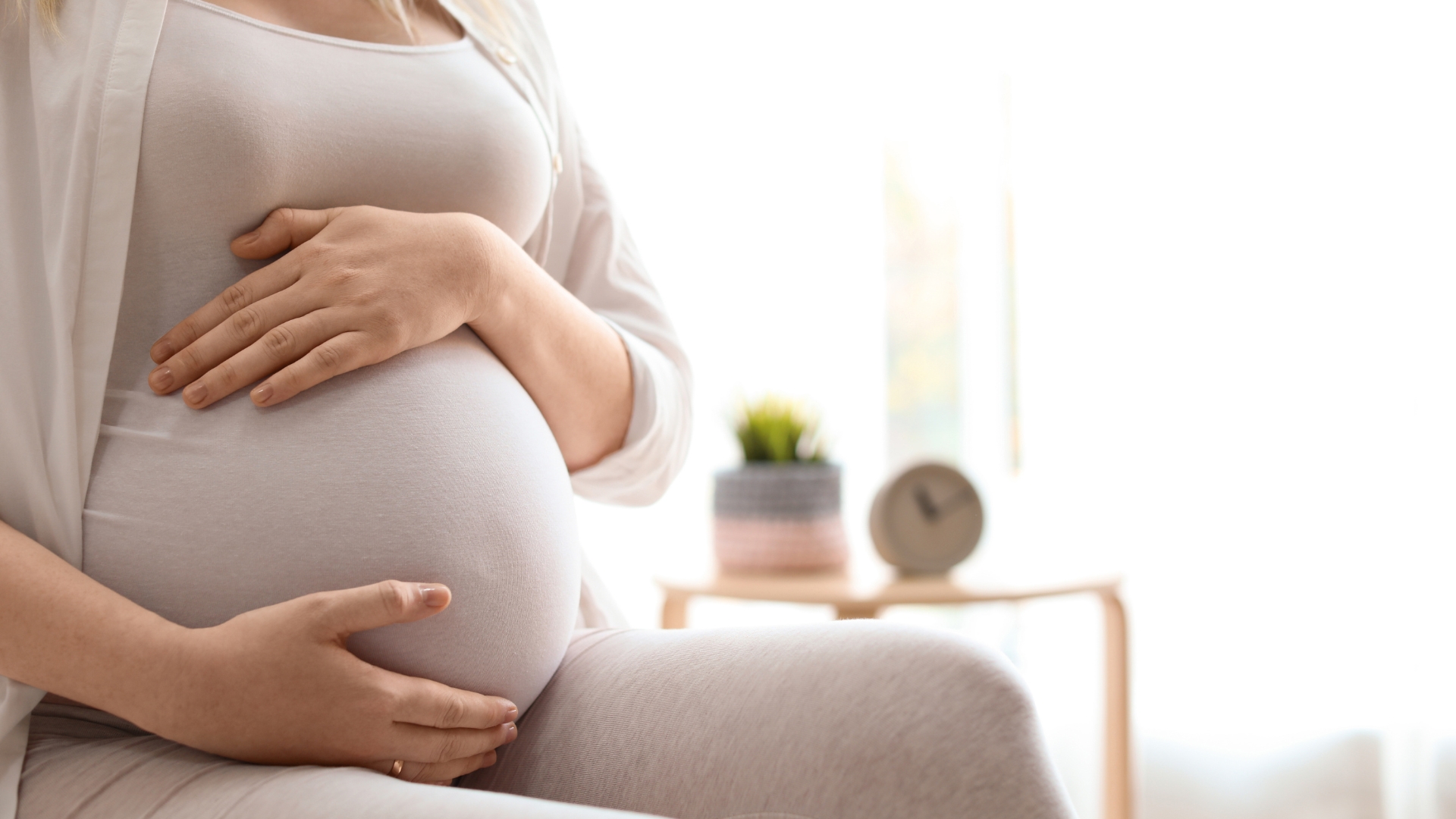 Mulher grávida segurando a barriga em casa, representando os resultados de tratamentos de fertilidade e fatores que influenciam a taxa de sucesso da IVM.